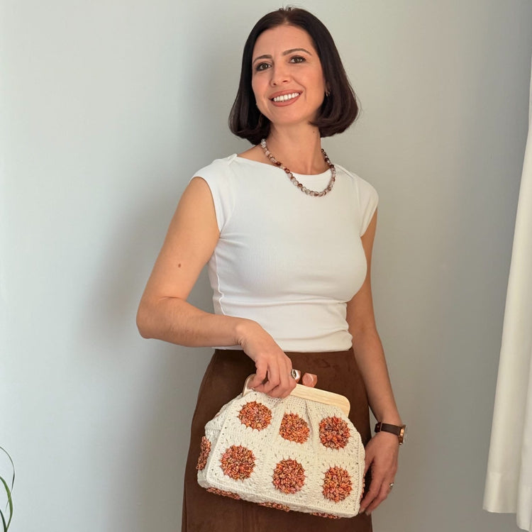 Woman holding a white handbag with brown floral patterns against a plain background