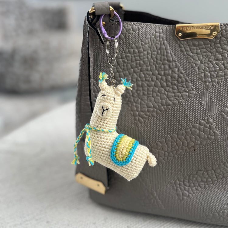 Llama keychain attached to a gray handbag on a light surface.