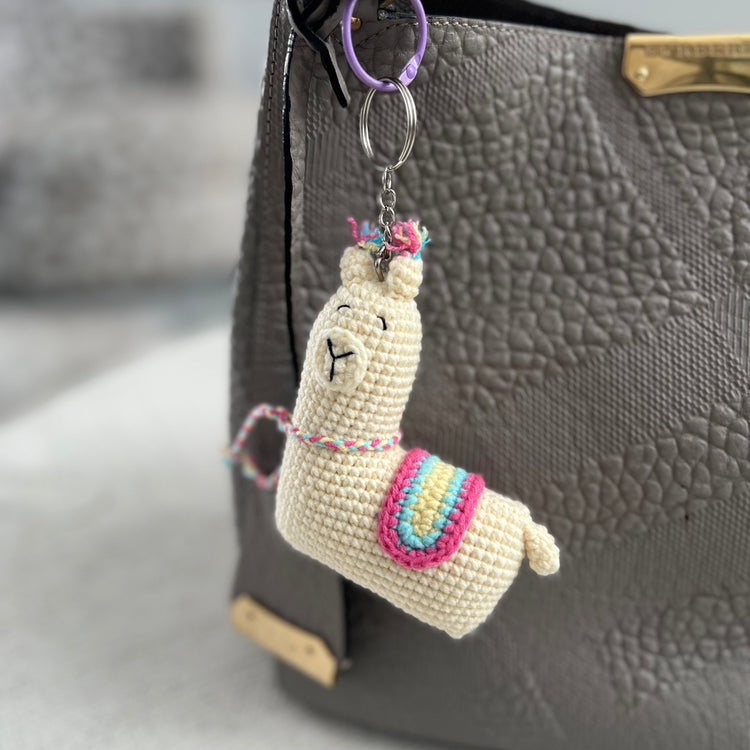 Crocheted llama keychain attached to a gray textured bag.